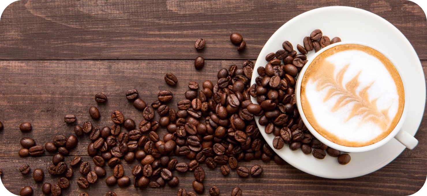 A latte with leaf art beside scattered coffee beans on a wooden table